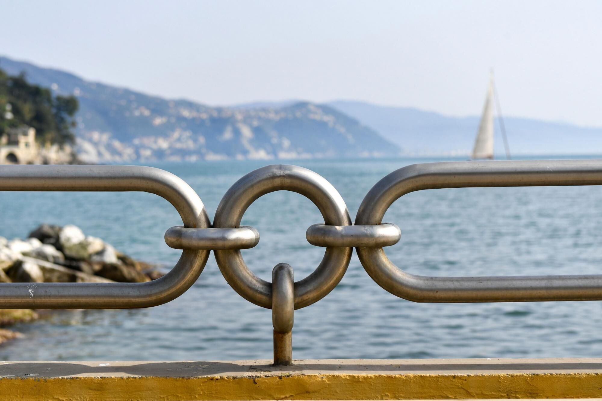 A metal railing with a view of a coastal landscape, including a bridge and distant hills.