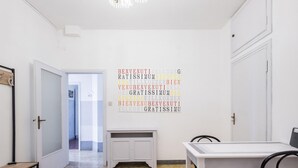 Ein Hotelzimmer mit weißer Tür, Kleiderständer, kleinem Tisch und Wandbild mit Schriftzug.