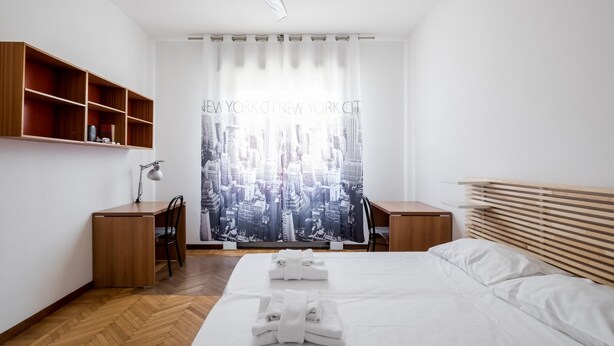 Ein Hotelzimmer mit Bett, Schreibtisch, Stuhl, Deckenventilator und Fenster mit Blick auf die Stadt.