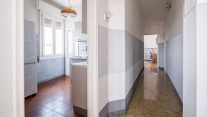 Ein enger Flur mit einer Küchenzeile links, inklusive Kühlschrank, Spüle und Fenster.