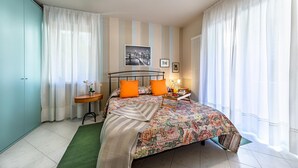 A bedroom with a bed, curtains, a side table, a lamp, and a framed picture on the wall. - Al Vittoriale 3 by Wonderful Italy (Gardone Riviera)