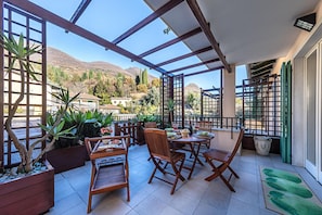 A covered patio with wooden furniture, potted plants, and a view of a mountainous landscape. - Al Vittoriale 3 by Wonderful Italy (Gardone Riviera)