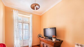 Une pièce avec un téléviseur posé sur un meuble en bois, une fenêtre avec des rideaux et un luminaire au plafond.