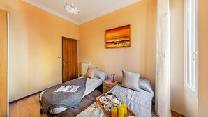 Une chambre d’hôtel avec deux lits, une porte en bois, un tableau et un plateau de petit-déjeuner posé sur le sol.