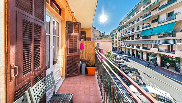 Un balcon donnant sur une rue animée, une poubelle et un banc.