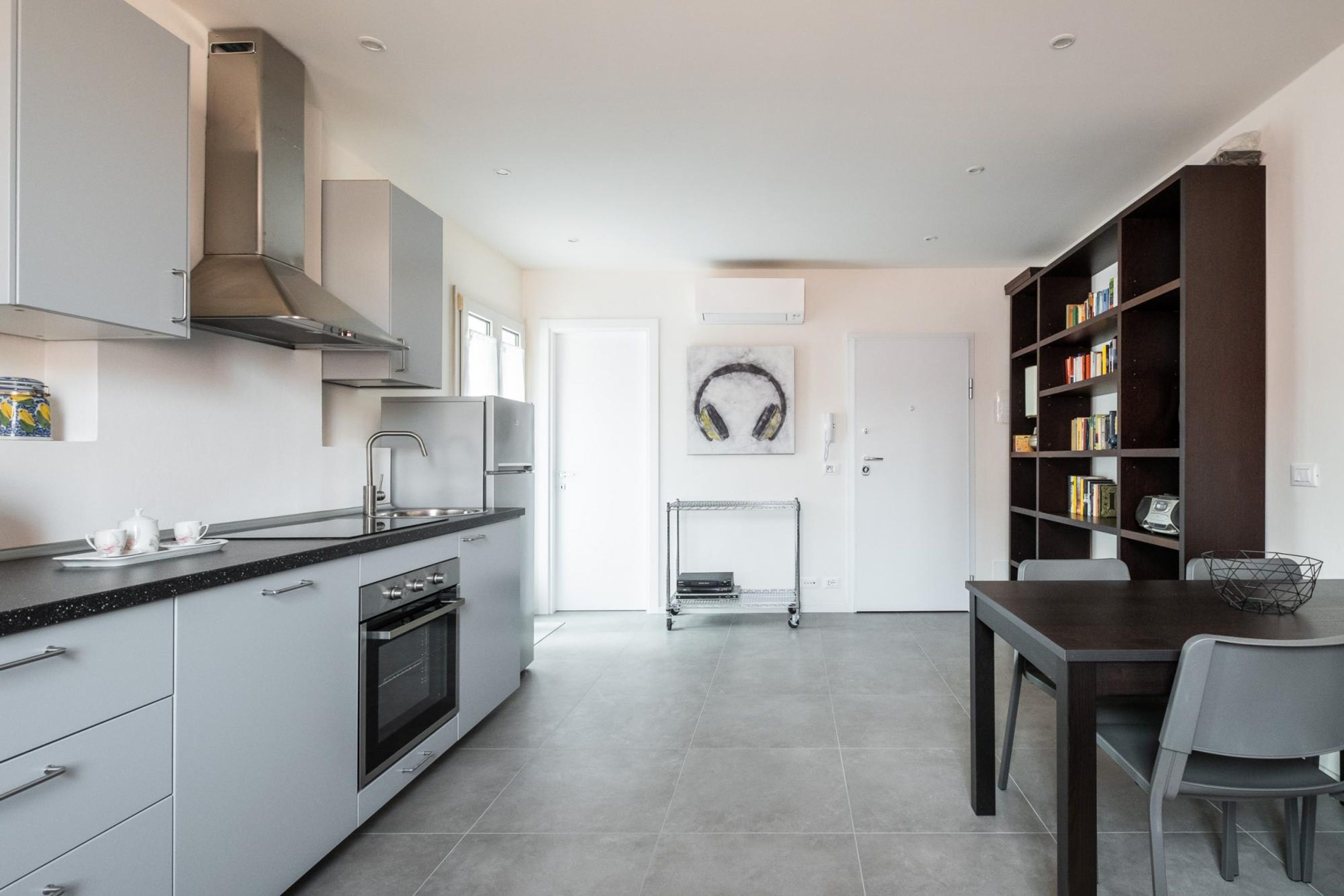 A modern kitchen with grey cabinetry, a stainless steel range hood, and a dining area with a dark wooden table and chairs.