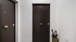 A hallway with two dark wooden doors, a small trash bin with umbrellas, and a white wall.