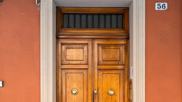 A double wooden door with a white frame, set in a building with an orange exterior wall.