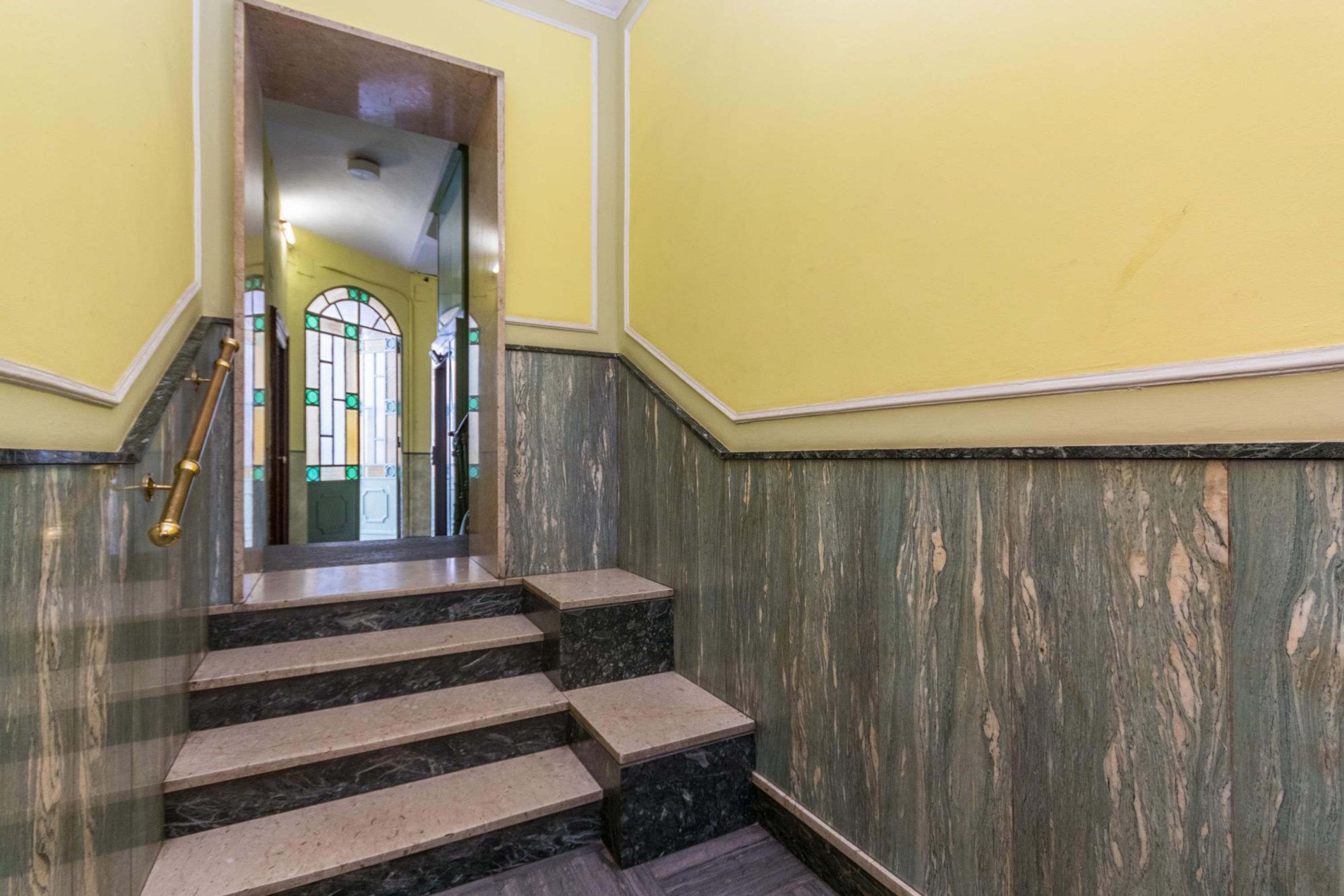 Een trap met marmeren treden en een houten leuning, die leidt naar een kamer met een gele wand en een houten paneeldecoratie.