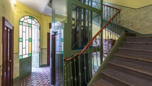 A staircase with a wooden handrail and green metal balusters, leading to a room with a patterned floor and a door with stained glass. - Sunny Apartment by Wonderful Italy (Turin)