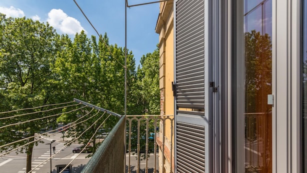A balcony with a view of a tree-lined street and a closed shop door. - Sunny Apartment by Wonderful Italy (Turin)