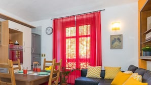 A cozy living room with a dining area, a sofa with yellow cushions, a potted plant, and a red curtain. - Sunny Apartment by Wonderful Italy (Turin)