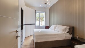 A bedroom with a bed, a wardrobe, a bedside table, a nightstand, a ceiling light fixture, and a window with a view of trees. - Vernazzola Family Apartment by Wonderful Italy (Genoa)