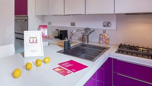 A modern kitchen with white cabinets, a stainless steel sink, and a gas stove. There are lemons on the counter and a welcome sign. - Vernazzola Family Apartment by Wonderful Italy (Genoa)