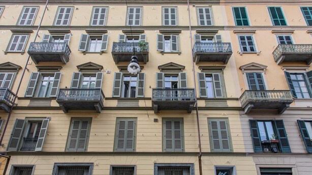 Un edificio de varios pisos con balcones, ventanas con contraventanas y una farola.