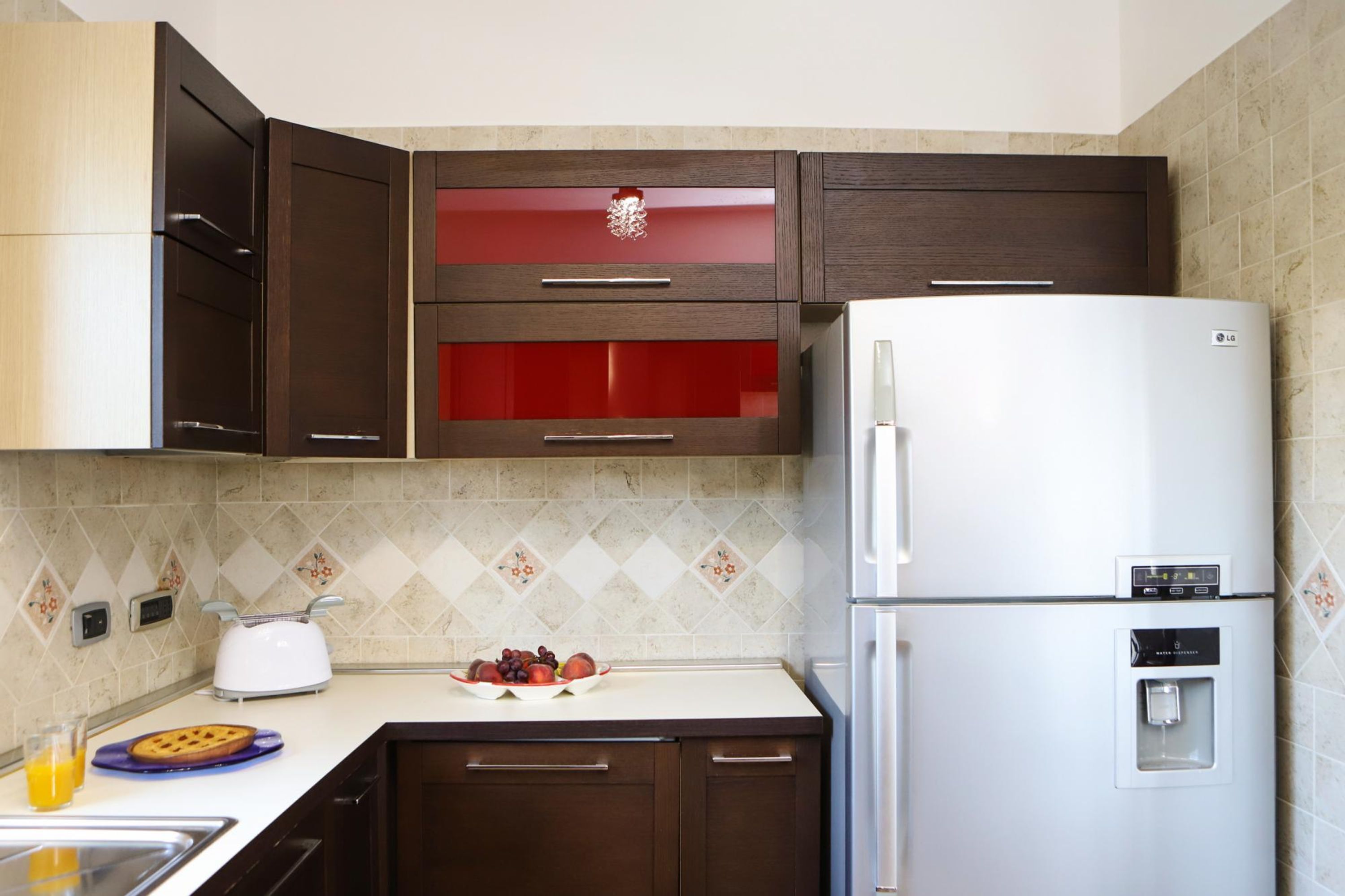 A kitchen with dark wooden cabinets, a white refrigerator, a toaster, and a fruit bowl on the counter.