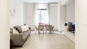 A modern living room with a sofa, dining table, chairs, a TV, and a window with curtains. - Carignano Design Apartment 9 by Wonderful Italy (Genoa)