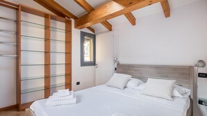 A bedroom with a wooden ceiling, a bed with white bedding, and a glass shelving unit. - Chez Cristina by Wonderful Italy (Bologna)
