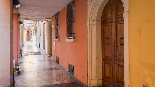 A corridor with a wooden door and windows, leading to a building with a yellow wall and an arched entrance. - Chez Cristina by Wonderful Italy (Bologna)