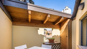 A wooden pergola with a table and chairs underneath, a potted plant, and a view of buildings in the background. - Chez Cristina by Wonderful Italy (Bologna)