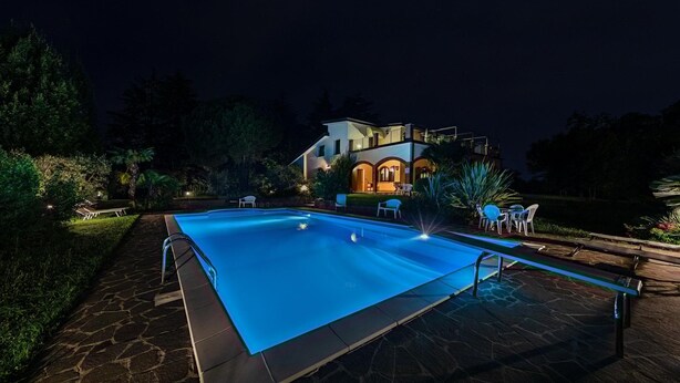 A swimming pool with a stone deck, a house with a lighted facade, and outdoor furniture. - Daller Bianca - BK in Soiano del Lago (Soiano del Lago)