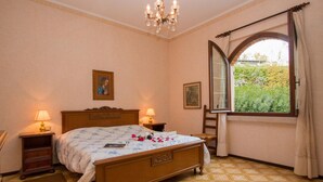 A bedroom with a wooden bed, two bedside tables with lamps, a large window with curtains, and a view of greenery outside. - Daller Bianca - BK in Soiano del Lago (Soiano del Lago)
