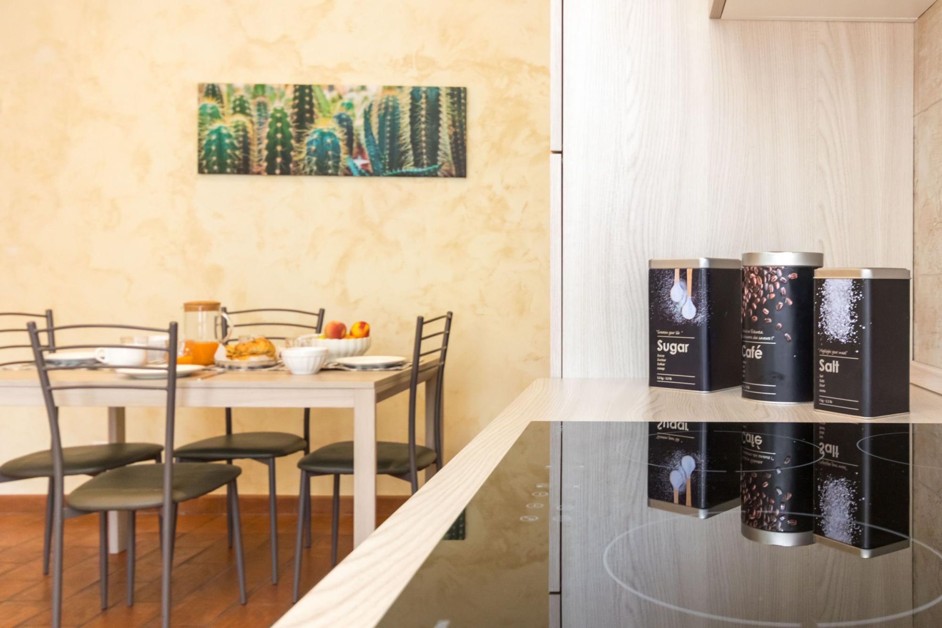 A modern kitchen with a dining table set for two, a painting on the wall, and three black containers labeled with food items.