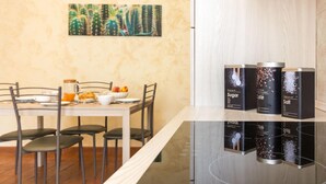 Uma cozinha moderna com uma mesa de jantar posta para dois, um quadro na parede e três recipientes pretos identificados com alimentos.