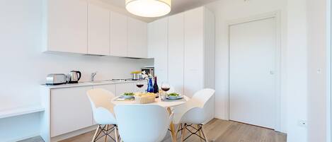A modern kitchen with white cabinets, a dining table with four chairs, and a hanging light fixture.