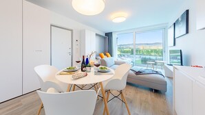 Un espace de salle à manger moderne, avec une table ronde, des chaises blanches et une vue sur l’extérieur grâce à de grandes fenêtres.