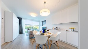 Une cuisine moderne avec des meubles blancs, une table à manger entourée de chaises blanches et une grande fenêtre donnant sur l’extérieur.