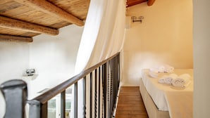 Una habitación con techo de madera, una cama con ropa blanca y un pequeño estante con un objeto decorativo.