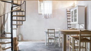 Una habitación con una escalera de caracol, una mesa de comedor con sillas, un armario y una ventana con cortinas.