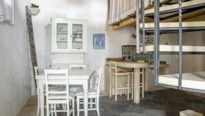 Una habitación con una mesa y sillas blancas, un armario, un salpicadero de azulejos y una cama litera con escalera de madera.