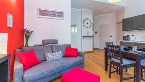A modern living room with a grey sofa, red cushions, a cityscape painting, a wall clock, and a dining area with wooden chairs and a table. - Casa Boccaccio by Wonderful Italy (Turin)