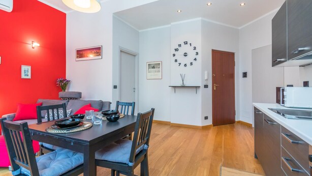 A modern living space with a dining area, a kitchen, and a red accent wall. - Casa Boccaccio by Wonderful Italy (Turin)