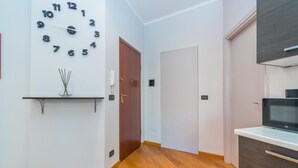 A hallway with a clock, a wooden door, a white door, and a microwave on a counter. - Casa Boccaccio by Wonderful Italy (Turin)
