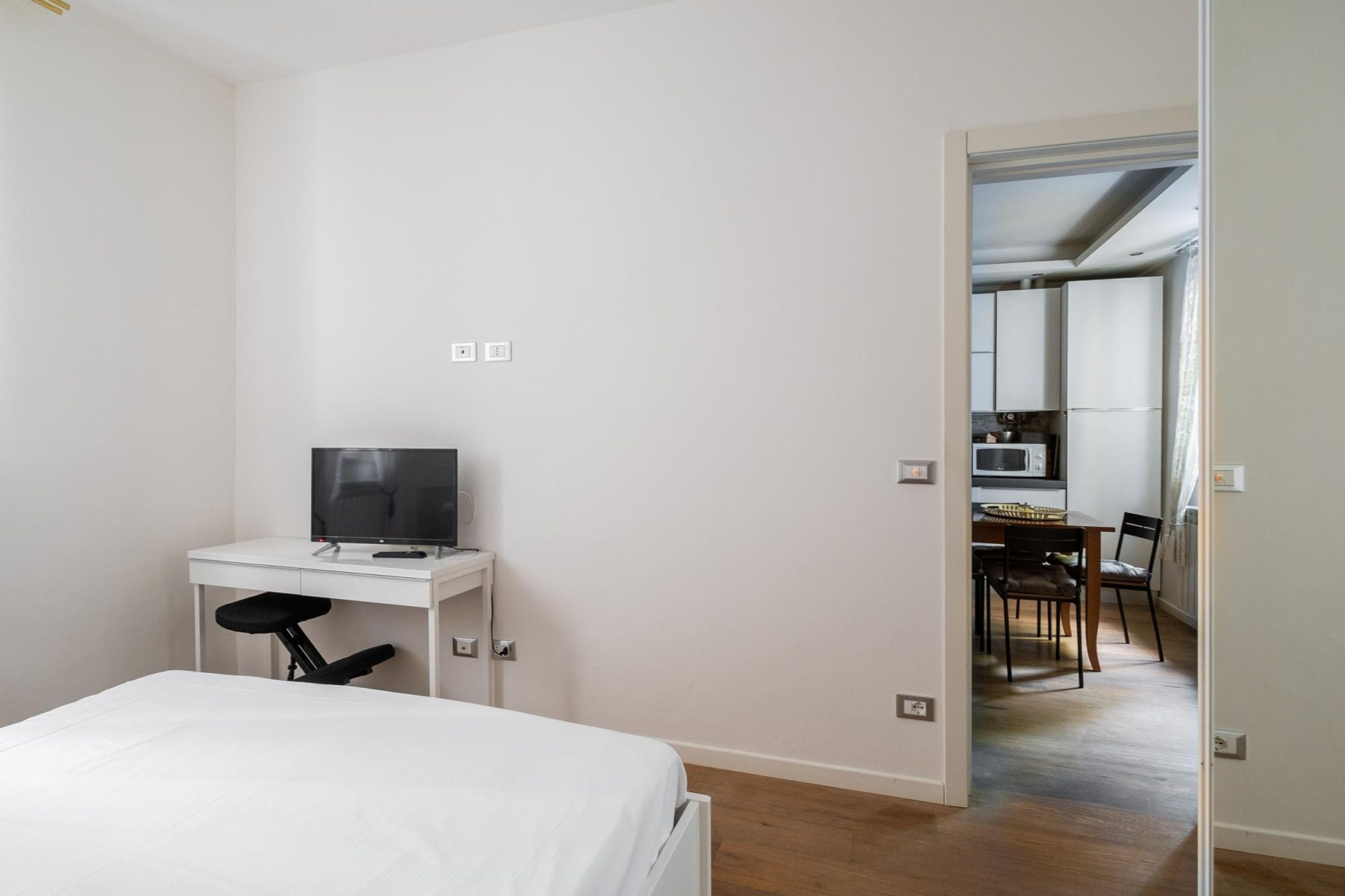 Un dormitorio con una cama, un escritorio con computadora y vistas a una zona de cocina.