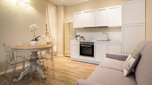 A modern kitchen with white cabinets, a dining table with clear chairs, and a sofa with a cushion.