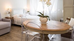 A modern bedroom with a bed, a round dining table with chairs, a potted orchid, and a nightstand with a lamp.