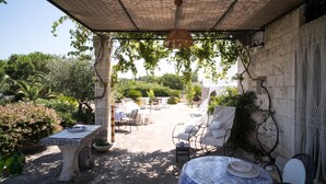Une terrasse extérieure avec des tables et des chaises en pierre, ainsi qu’un luminaire suspendu.