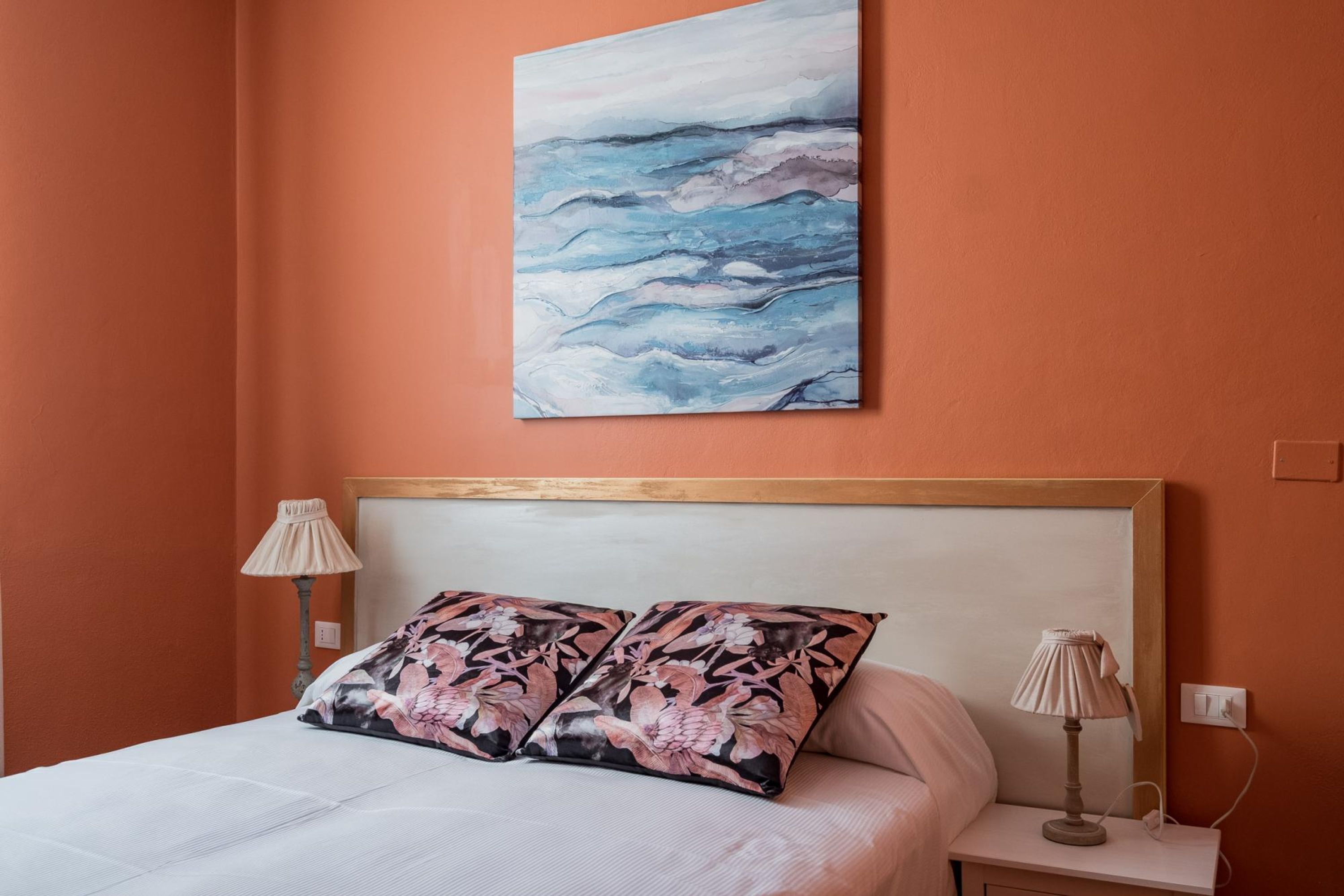 A bedroom with a bed, two pillows, a nightstand, a lamp, and a painting on the wall.