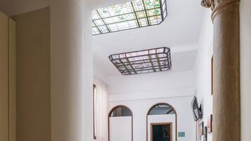 A spacious interior with a high ceiling, a dining area with wooden chairs, a large column, and a stained glass window.