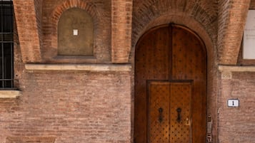 A brick building with a large wooden double door, arched windows, and a small window with bars.