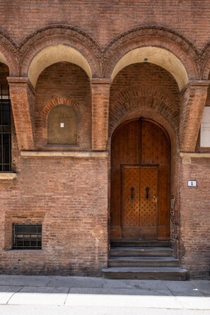 A brick building with a large wooden double door, arched windows, and a small window with bars. - Rolandino Apartment by Wonderful Italy (Bologna)