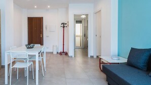 Una sala moderna con un sofá gris, una mesa de comedor con sillas blancas y un perchero rojo.