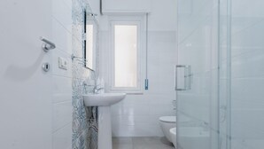 Un baño moderno con un lavamanos blanco, cabina de ducha con mampara de vidrio y un inodoro.