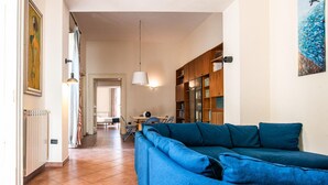 A living room with a blue sofa, a wooden bookshelf, and a dining area with a table and chairs. - Maiorani Family Apartment nel Centro di Napoli (Naples)