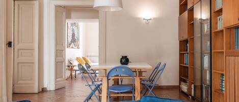 A room with a dining table, chairs, a blue sofa, a white lamp, and a bookshelf.