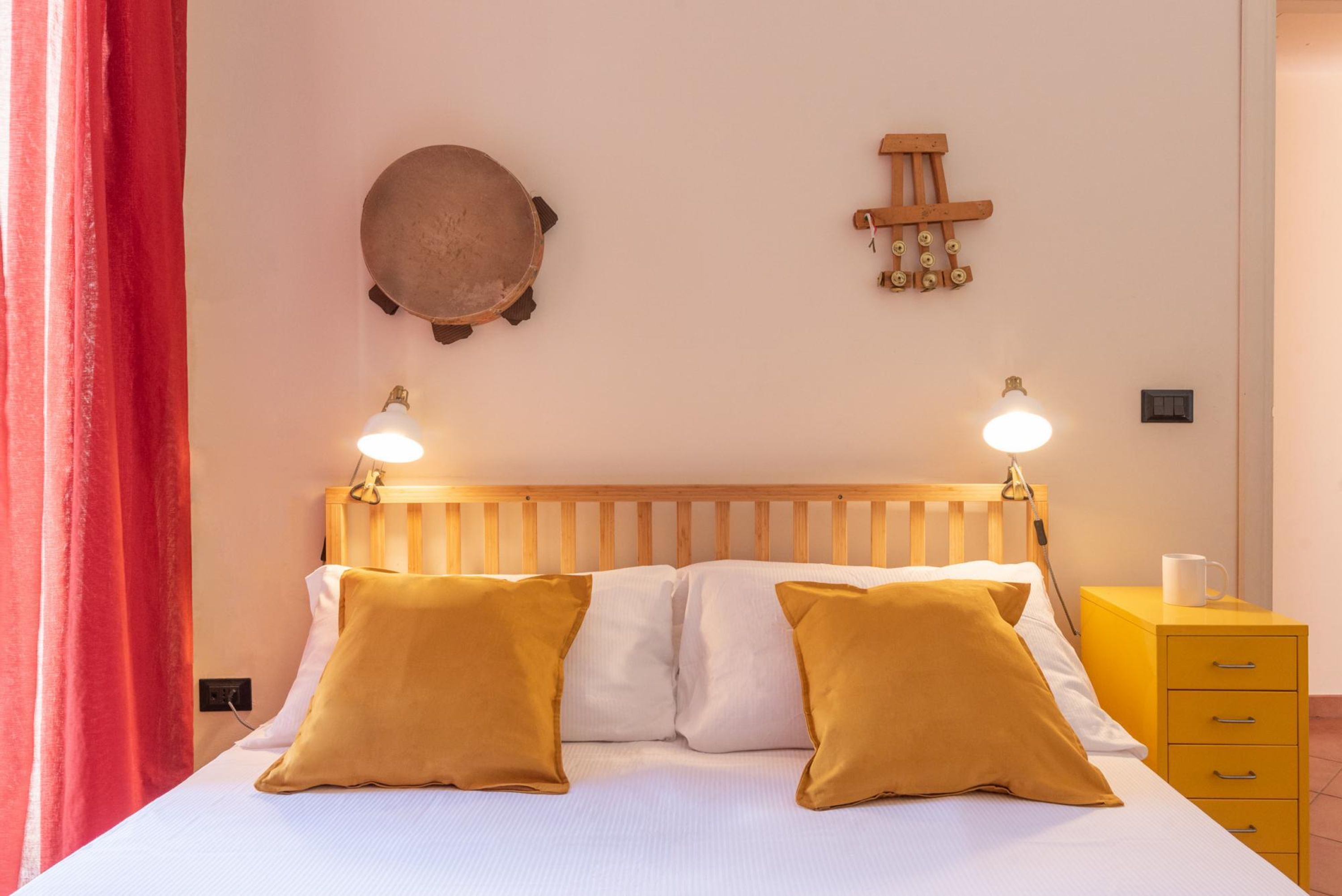 Un lit avec deux oreillers, une tête de lit en bois, des lampes de chevet, une horloge murale et une table de chevet jaune sur laquelle se trouve une tasse.